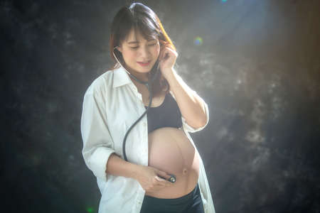 pregnant woman is listening to her tummy with stethoscope in her hands and happy