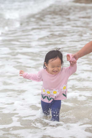 little girl cheerful smile run on the beach with mother's hold handの写真素材