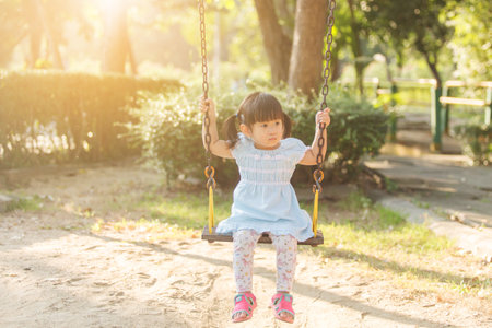 Little girl having to play swing first time in the playground , the eveningの写真素材