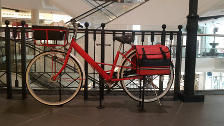 A red bicycle with white wheels parked on a dark brown tiled floor, behind a black steel grillの写真素材