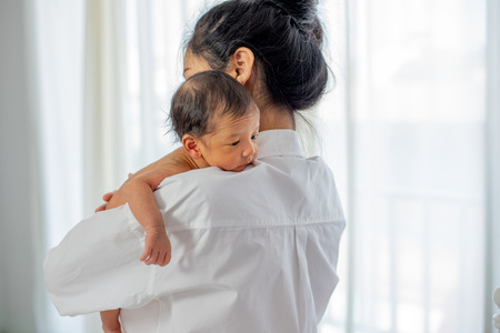 Asian mother with white shirt place upon the shoulder of little newborn baby after give milk and the baby look sleepyの写真素材
