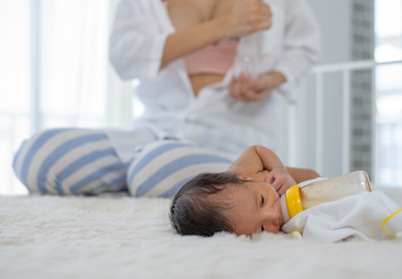 White shirt mother use breast milk pump to get breast milk and sitting near the sleeping newborn on white bedの写真素材