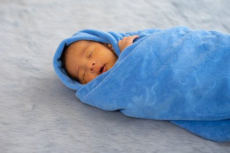 Little newborn baby is wrapped with blue towel and the baby is sleeping on gray carpetの写真素材