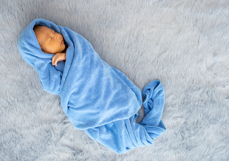 Little newborn baby is wrapped with blue towel and the baby is sleeping on gray carpet