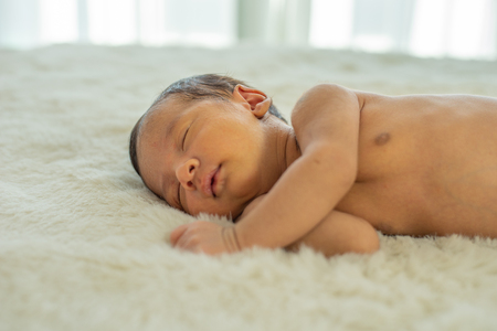 Close up view of Asian young newborn baby is sleeping and smile on white bed in the bedroom with soft lightの写真素材
