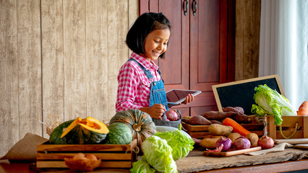 Asian young little girl with smiling use tablet to check the list of various vegetable on table in the kitchenの写真素材