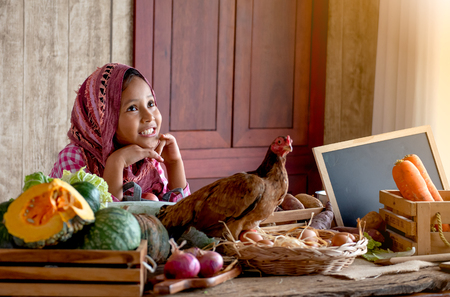 Asian little young girl look forward and smile among various types of vegetable on the table in her kitchenの写真素材