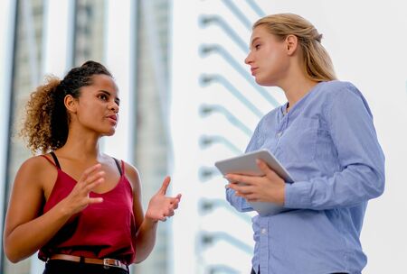 One mixed race girl stand and discuss with white caucasian girl who is holding tablet.の写真素材
