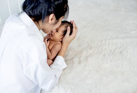 White shirt Asian mother is kissing and holding newborn baby near fluffy bed with concept love and careful for babyの写真素材