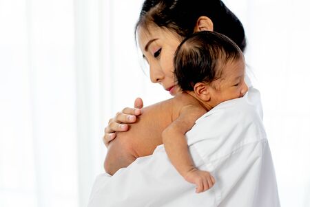 Asian mother with white shirt place upon the shoulder of little newborn baby after give milk and the baby look sleepy.の写真素材