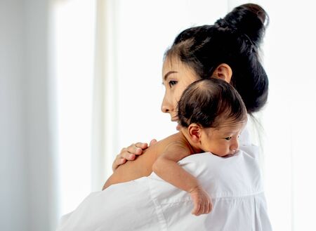 Asian mother with white shirt place upon the shoulder of little newborn baby after give milk and the baby look sleepy.の写真素材