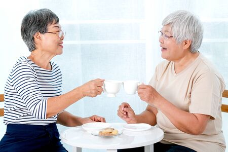 Two Asian elderly women drink tea together in the morning and also have some cookies, they are smile and talk about some stories.の写真素材