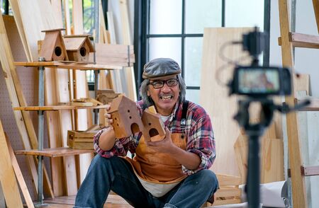 Asian old craftsman present his wood product in front of the camera and look like sell it online.の写真素材