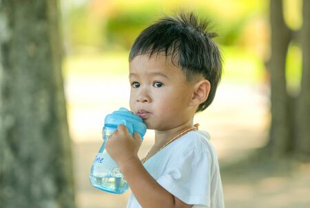 Little boy drink water from blue bottle in the green garden with day light.の写真素材