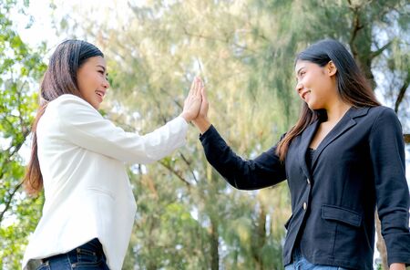 Two business girls touch their hands together or hi five in the garden with concept of the...