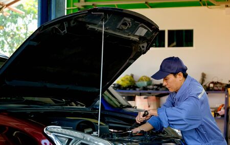 Asian automotive mechanic with blue uniform use wrench to fix the problem in part of engine around...