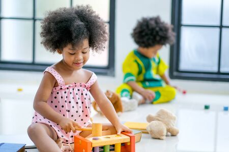 Portrait of one young African mixed race girl is playing with toys in front of the other african boy and look like she enjoy and happy with this activity.の写真素材