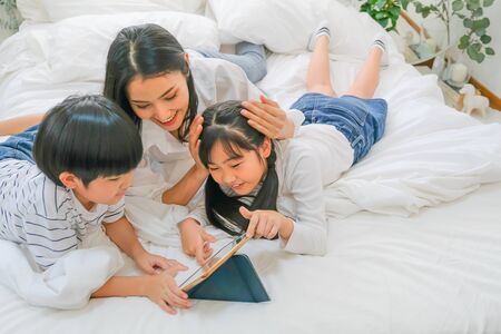 Soft blur of Asian mother and her children have fun with tablet in bedroom.