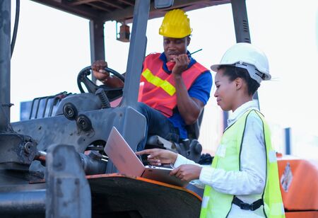 African technician worker woman use laptop to discuss with her team who stay on tractor in cargo...