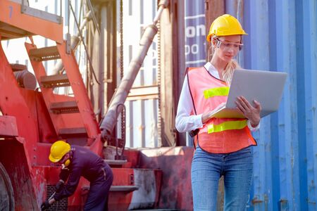 Beautiful technician or worker in cargo shipping area work with laptop and the other is working as background.の写真素材