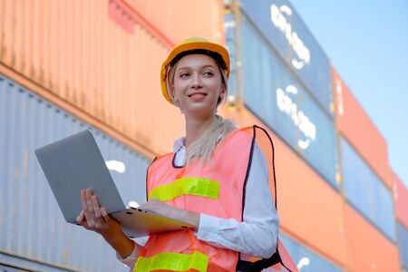 Portrait of beautiful technician use laptop in front of cargo containers with day light.