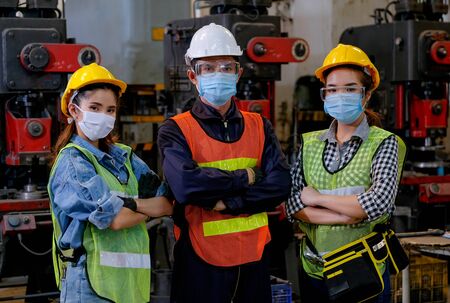 Group of man and woman workers with mask stand with confident action in the factory workplace and various machine as background.の写真素材