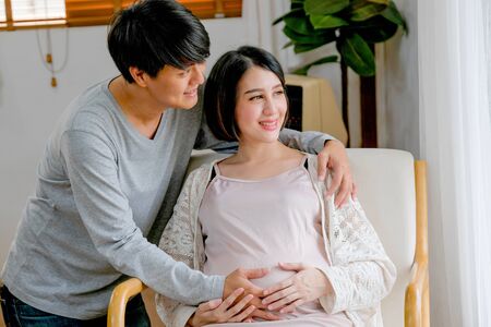 Asian man and pregnant woman look outside through glass windows with morning light.の写真素材