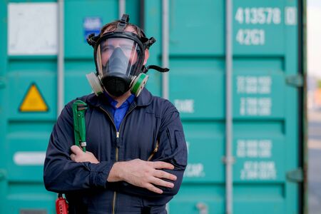 Technician or worker with chemical mask stand and hold wrench in front of green container and look confident.の写真素材