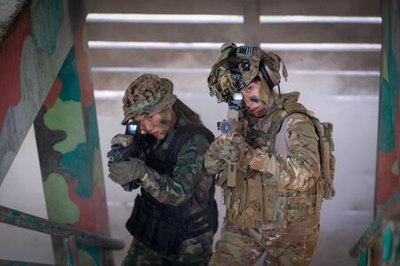 Two of woman soldiers hold gun and walk through step and go up to top of defensive base with the...