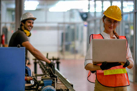 Pretty engineer or technician or worker woman hold the laptop and her co-worker stand and smile in the background and they work together in factory.の写真素材