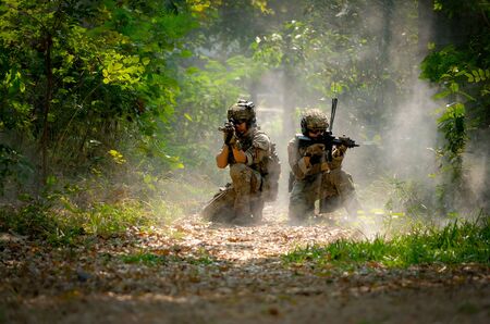 Two soldiers with the fighting uniform sit on the ground and point gun to target for the concept war...