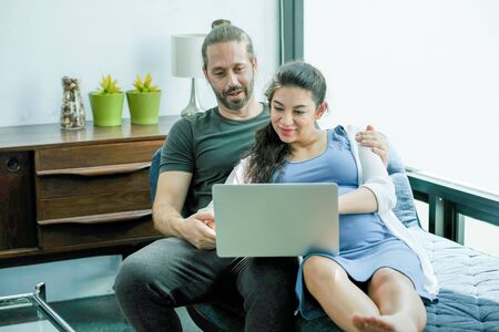 Man read some book for his pregnant wife in living room of their house during stay at home to prevent virus infection that pandemic in city. Concept of good activity at home for relaxation.の写真素材