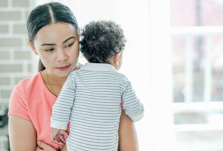Asian woman mother carry her African mixed race boy on shoulder and stand in front of balcony with...