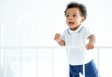 African American child boy stand near bed rail and he look happy by smiling and show teeth and look...