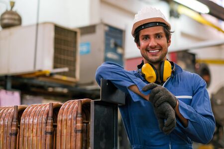 Factory worker man stand near copper tube or pipe and smiling in workplace look happy. Concept of...