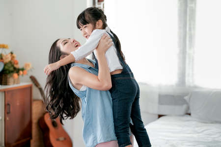 Asian little girl has fun with mother hold her with front side in bedroom with day light. Concept of...