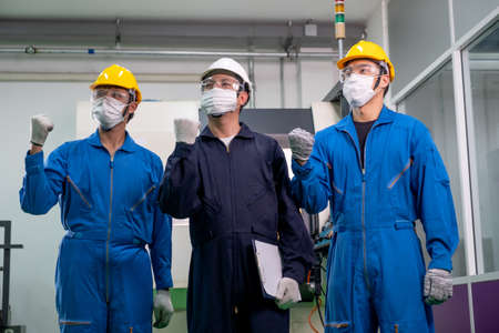 Three of factory workers men wearing mask stand with action of fighting and look to same direction. Concept of encouragement for working in industrial workplace to get better future in the business.の写真素材