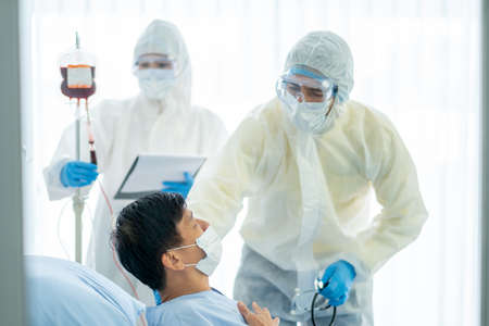 Doctor and nurse with full body cover suit take care and help Covid-19 infected patient in close...