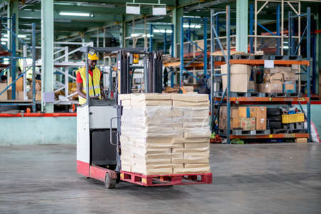 African American factory man or warehouse worker stand on forklift during work in workplace area to...