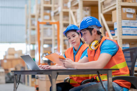 Warehouse man and woman or factory workers sit on chairs and discuss together about stock of products in workplace area. Concept of good management and happiness of staff work industrial business.の写真素材