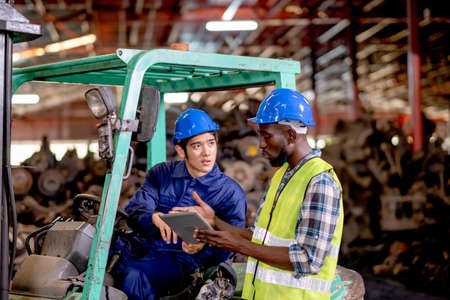 Asian technician or factory worker sit on forklift discuss about work using tablet with his...