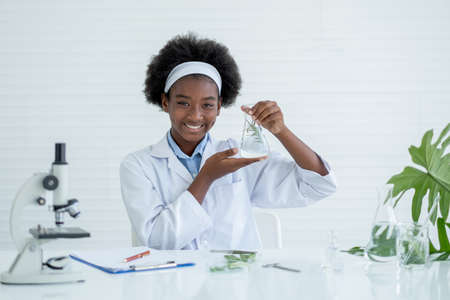 Young African American Scientist present flask with plant inside, smile and look to camera with other tools in laboratory and experiment with plant tissue science concept.の写真素材