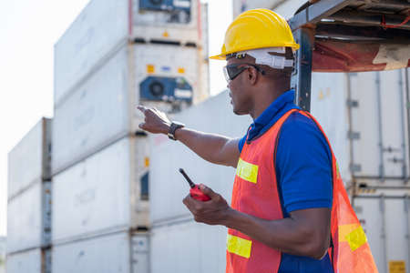 African American foreman or cargo container worker hold walkie talkie and point to front direction...