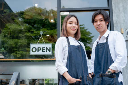 Two Asian barista or coffee maker man and woman stand with confidence action also look at camera and smile in front of coffee shop with day light.の写真素材