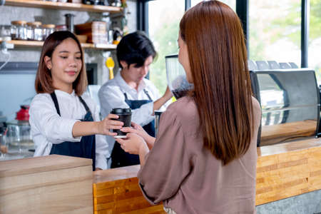 Barista girl or coffee maker give cup of coffee to her customer woman in coffee shop. Happy working with small business and sustainable concept.の写真素材