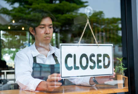 Barista or coffee maker man hold banner of closed for the symbol of no service for customer. Concept of virus pandemic and effect to people.の写真素材
