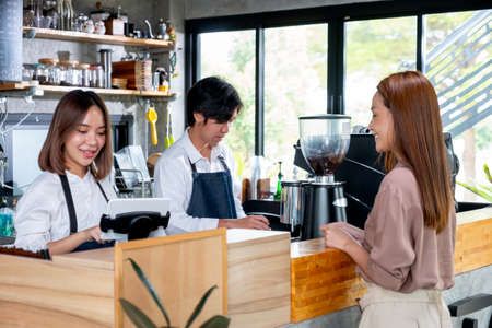Asian barista or coffee maker receive the order from customer woman while her co-worker prepare coffee by machine. Concept of good teamwork support small business system.の写真素材