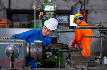 Asian factory worker woman look to part of the machine and inspect the function while her co-worker work with other machine in the background. Maintenance and check system support industrial business.の写真素材