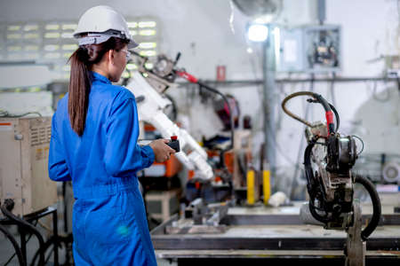 Back of factory worker woman hold controller to control metal welding robotic machine and work in workplace area. Industrial and technology support system help in working of employee concept.の写真素材