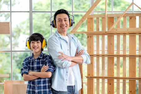 Portrait of Asian father and boy with mechanic headphone stand in front of woodwork and look at camera.の写真素材